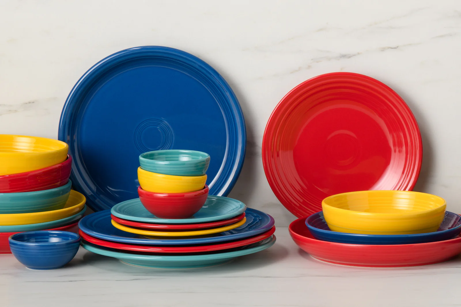 A colorful arrangement of plates and bowls in blue, red, yellow, and teal, set against a light marble background.